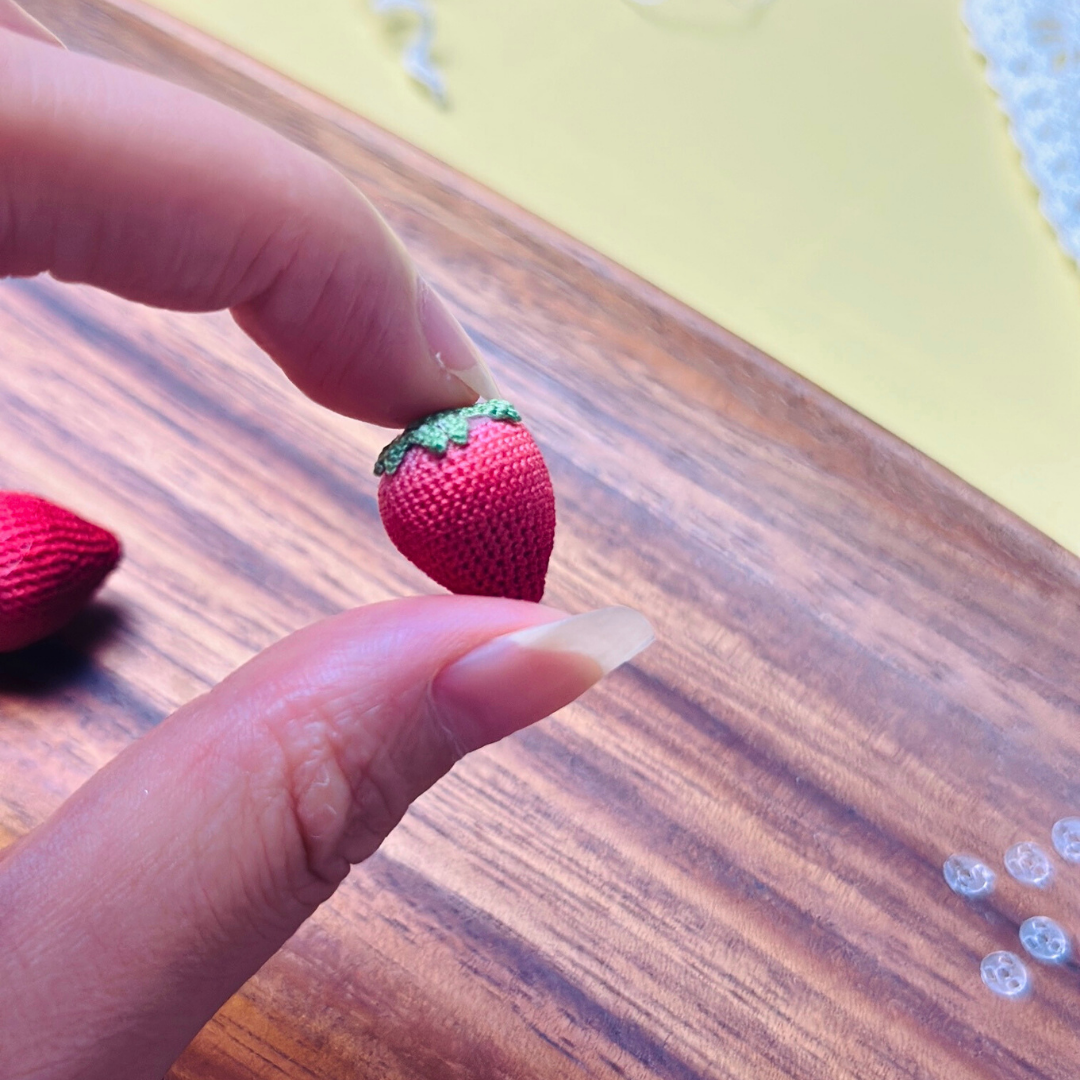 Single micro crochet strawberry held in hand, showing tiny berry size and structure