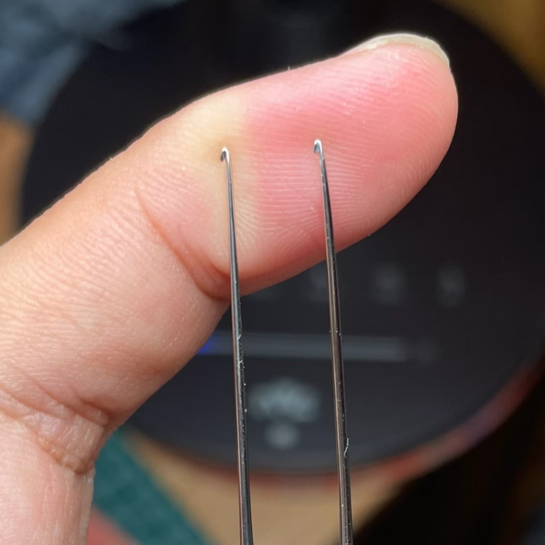 micro crochet hook resting on thumb to show ultra fine steel shaft and slim ergonomic rosewood handle