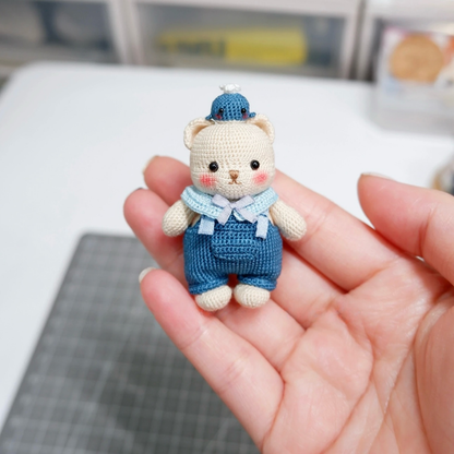 Small crocheted bear toy in blue overalls held in a hand with a blurred background