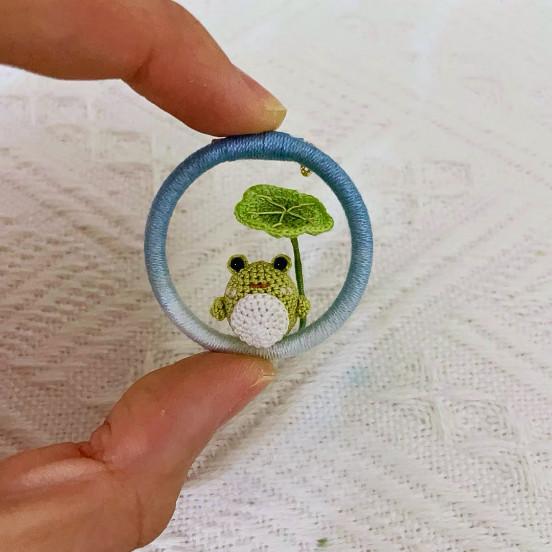 hand holding micro crochet frog brooch with green lotus leaf, anime style