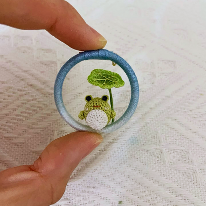hand holding micro crochet frog brooch with green lotus leaf, anime style