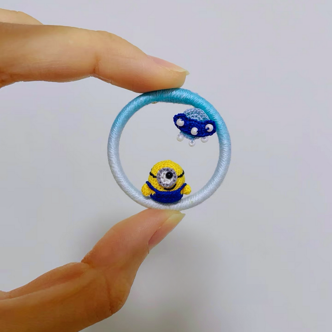 hand holding micro crochet minion inspired anime brooch with tiny UFO detail