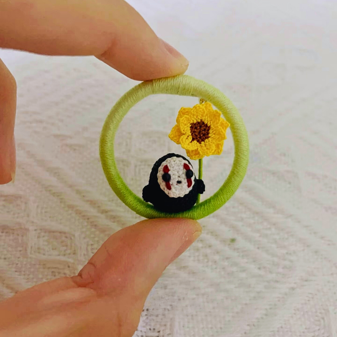 hand holding micro crochet No Face inspired anime brooch with sunflower detail