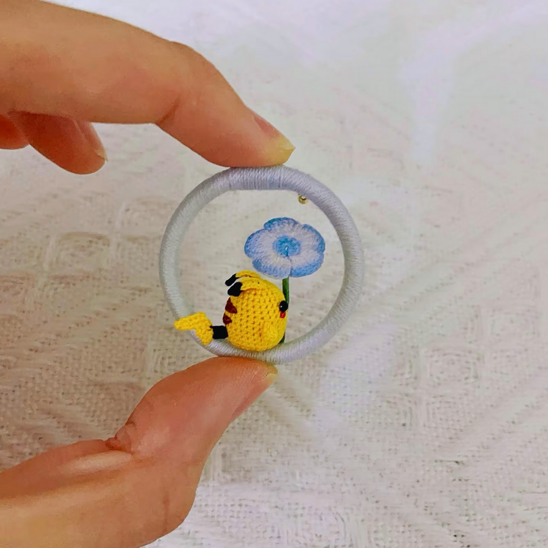 hand holding micro crochet Pikachu inspired anime brooch with green leaf on white background