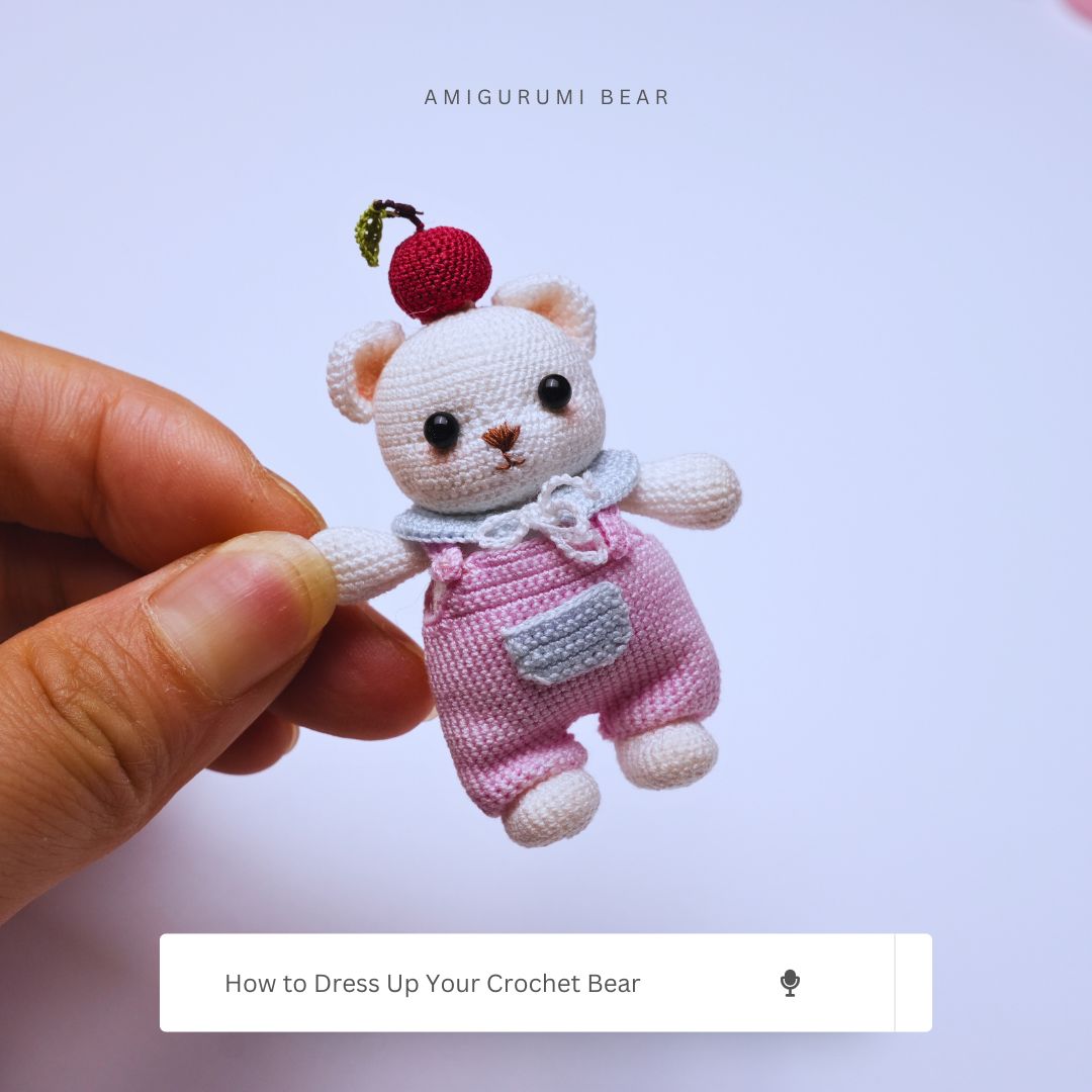 Small crocheted bear with a cherry on top held by a hand against a light purple background.