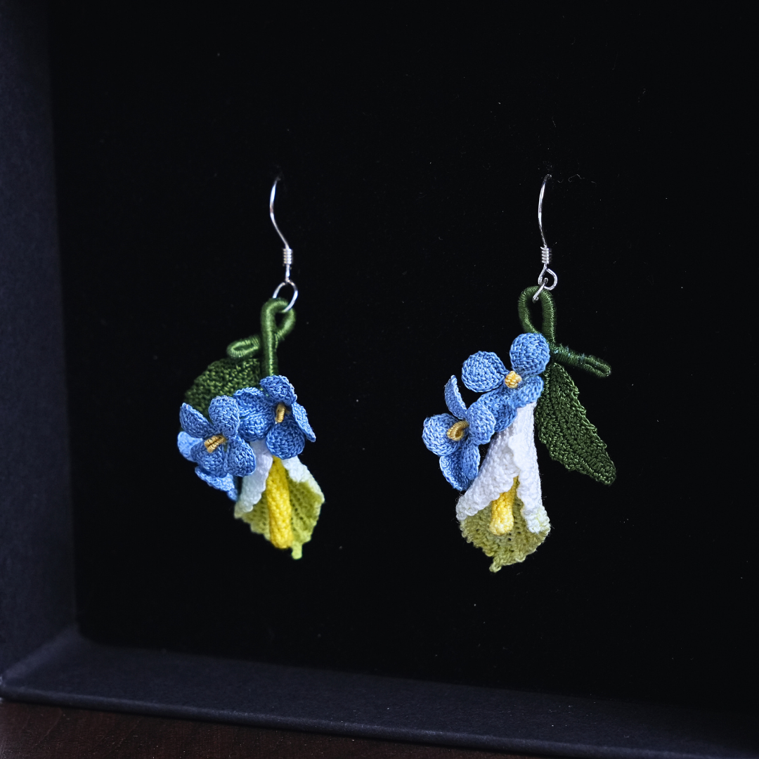 Micro crochet calla lily and blue flax earrings on black background, handmade floral earrings