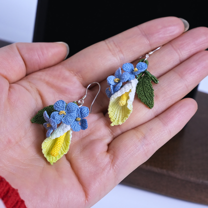 Micro crochet calla lily and blue flax earrings shown in hand for size reference