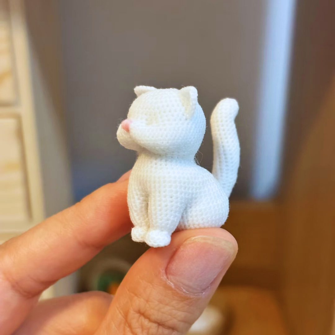 hand holding unpainted squat cat micro crochet charm base front view to show size and shape