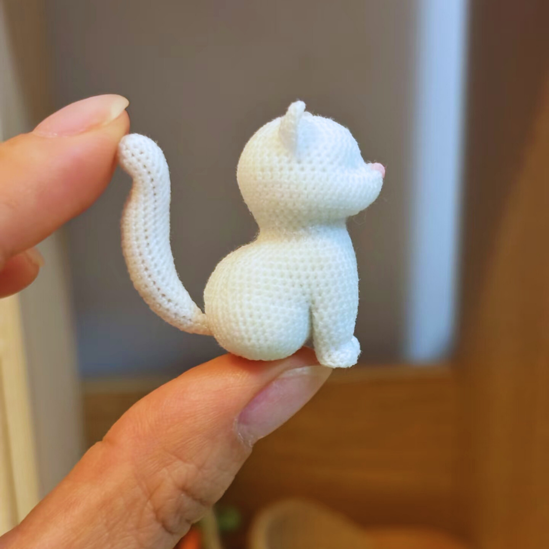 hand holding unpainted squat cat micro crochet charm base side view showing chubby profile and tail