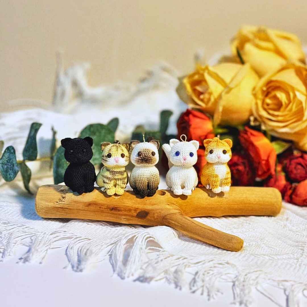 multiple micro crochet custom cat charms in different coat colours lined up on table, chubby squat cat design