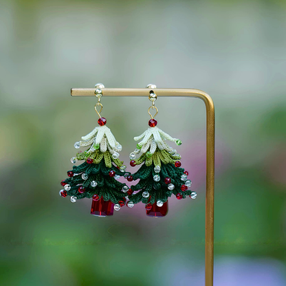 Short-style handmade micro crochet Christmas tree earrings displayed on a gold-colored stand, with layered green branches and red and clear bead accents.
