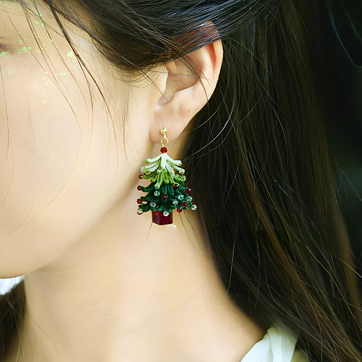 Short-style handmade micro crochet Christmas tree earring worn on the ear, showing its layered green branches and red and clear bead details.